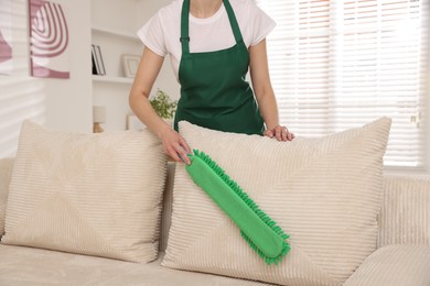 Photo of Janitor cleaning sofa with duster at home, closeup