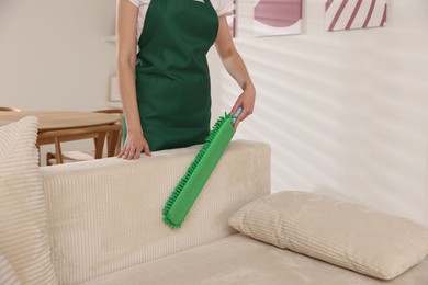 Photo of Janitor cleaning sofa with duster at home, closeup