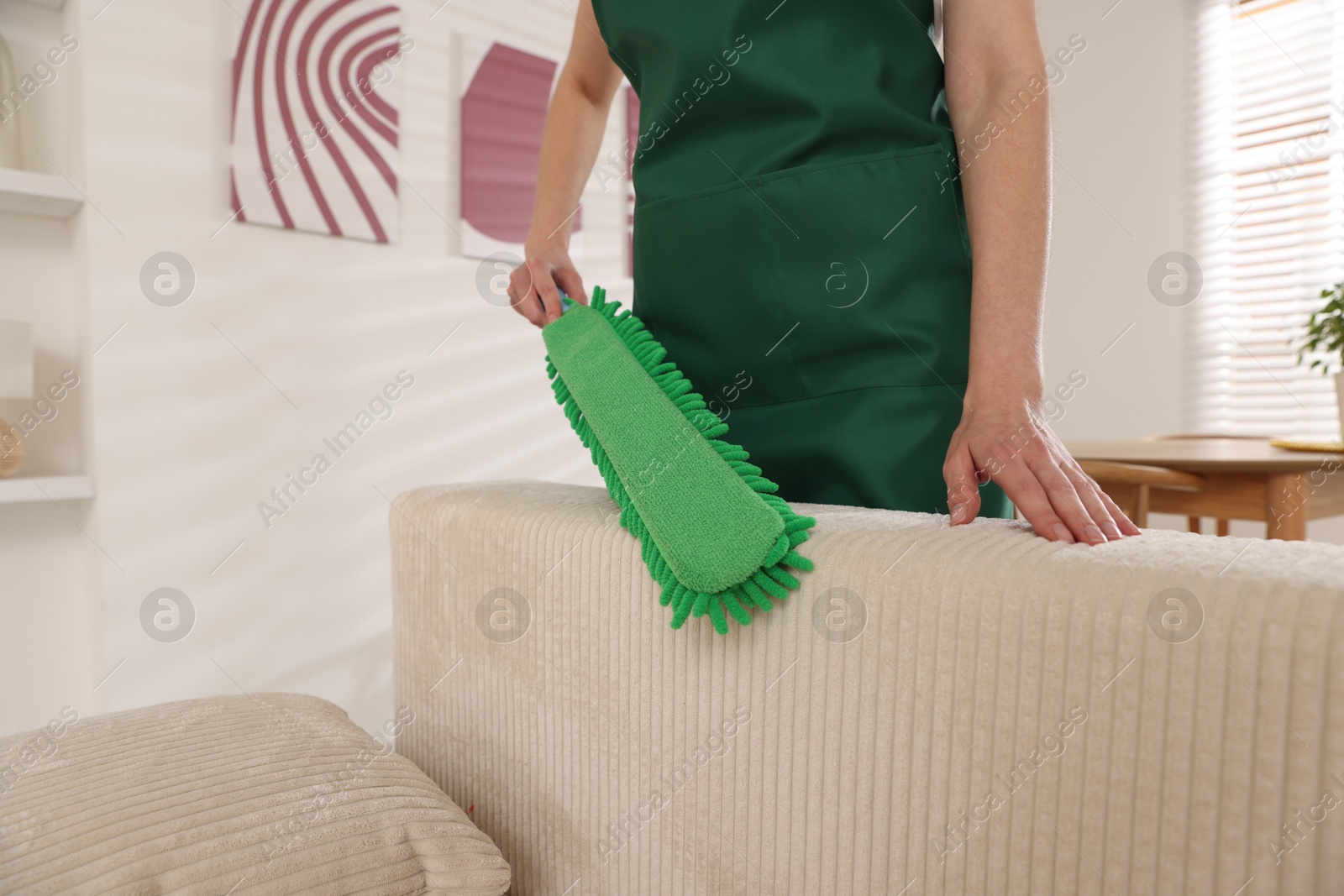 Photo of Janitor cleaning sofa with duster at home, closeup