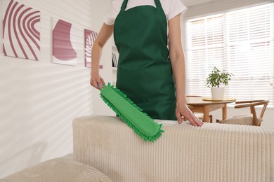 Photo of Janitor cleaning sofa with duster at home, closeup