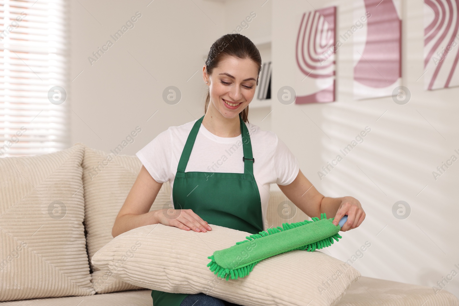 Photo of Janitor cleaning sofa cushion with duster at home