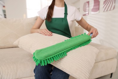 Photo of Janitor cleaning sofa cushion with duster at home, closeup