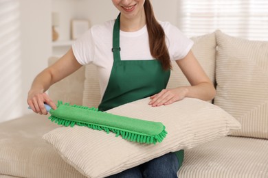 Janitor cleaning sofa cushion with duster at home, closeup