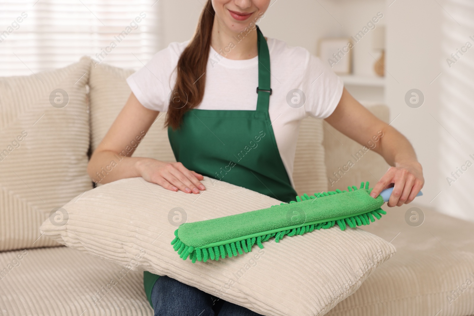 Photo of Janitor cleaning sofa cushion with duster at home, closeup