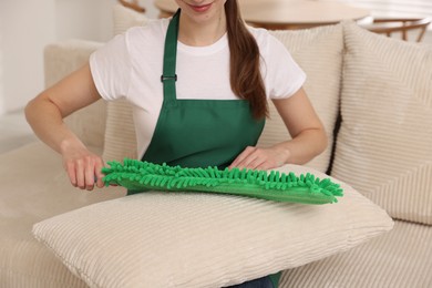 Photo of Janitor cleaning sofa cushion with duster at home, closeup