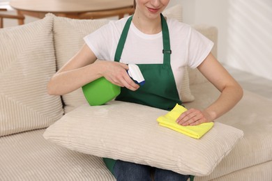 Photo of Janitor cleaning sofa with rag at home, closeup