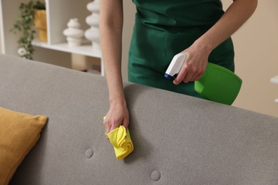 Photo of Janitor cleaning sofa with rag at home, closeup