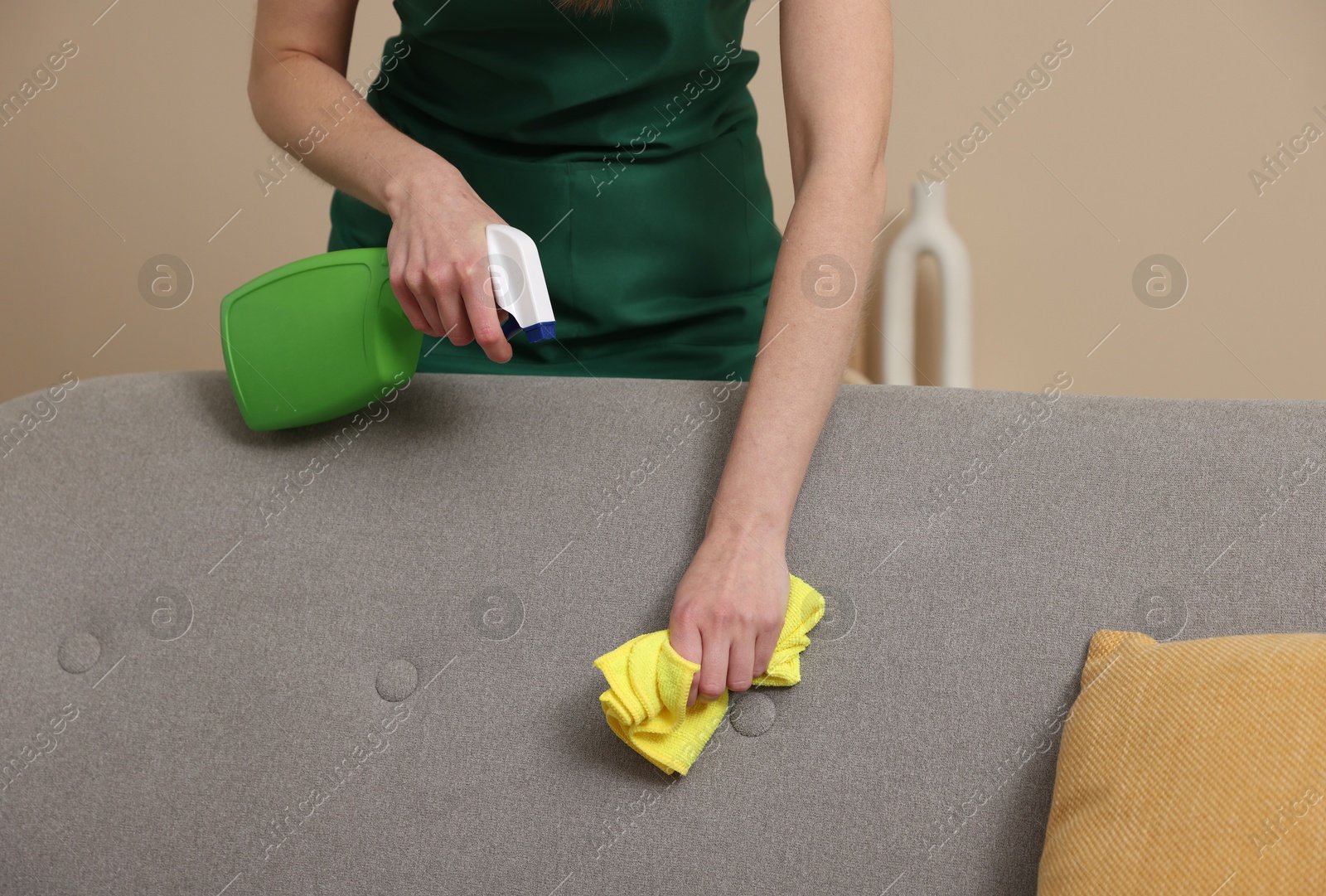 Photo of Janitor cleaning sofa with rag at home, closeup