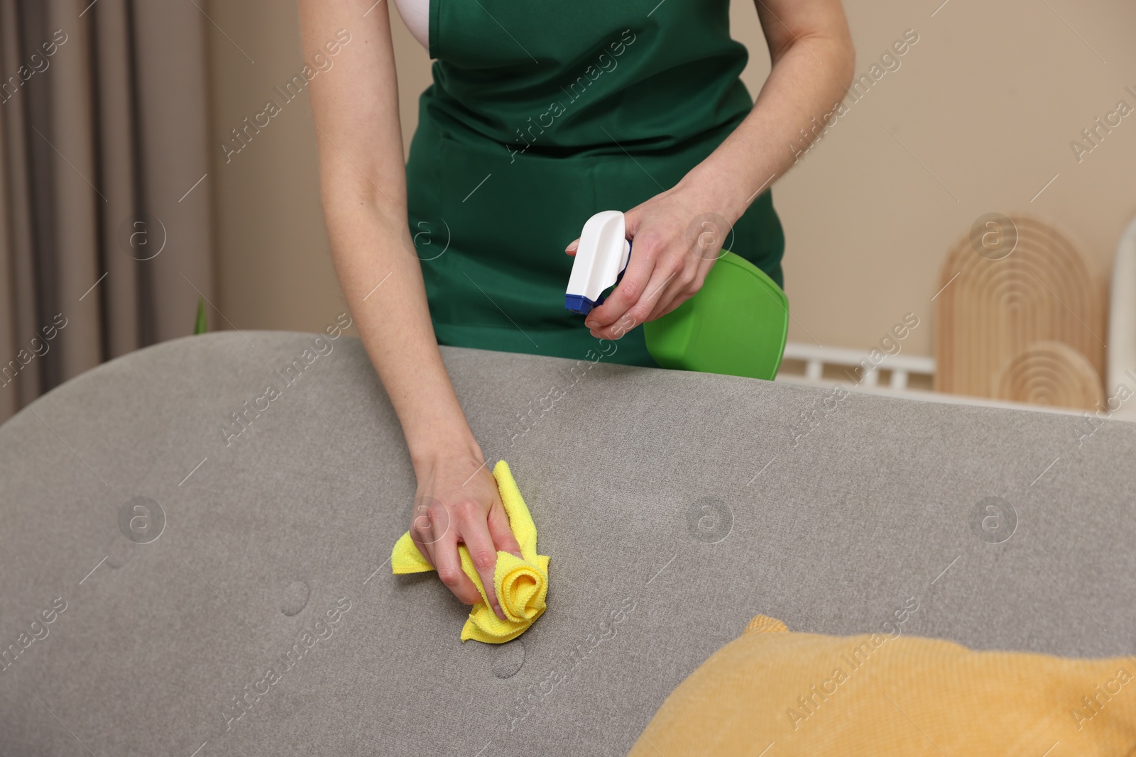 Photo of Janitor cleaning sofa with rag at home, closeup