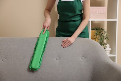 Photo of Janitor cleaning sofa with duster at home, closeup