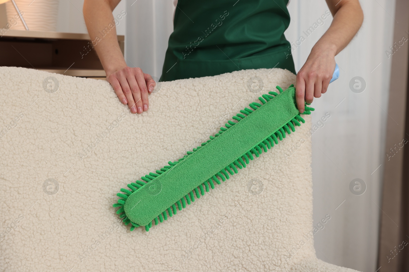 Photo of Janitor cleaning armchair with duster at home, closeup