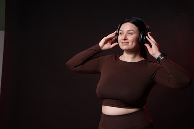 Photo of Plus size woman in gym clothes and headphones on black background with smoke, space for text