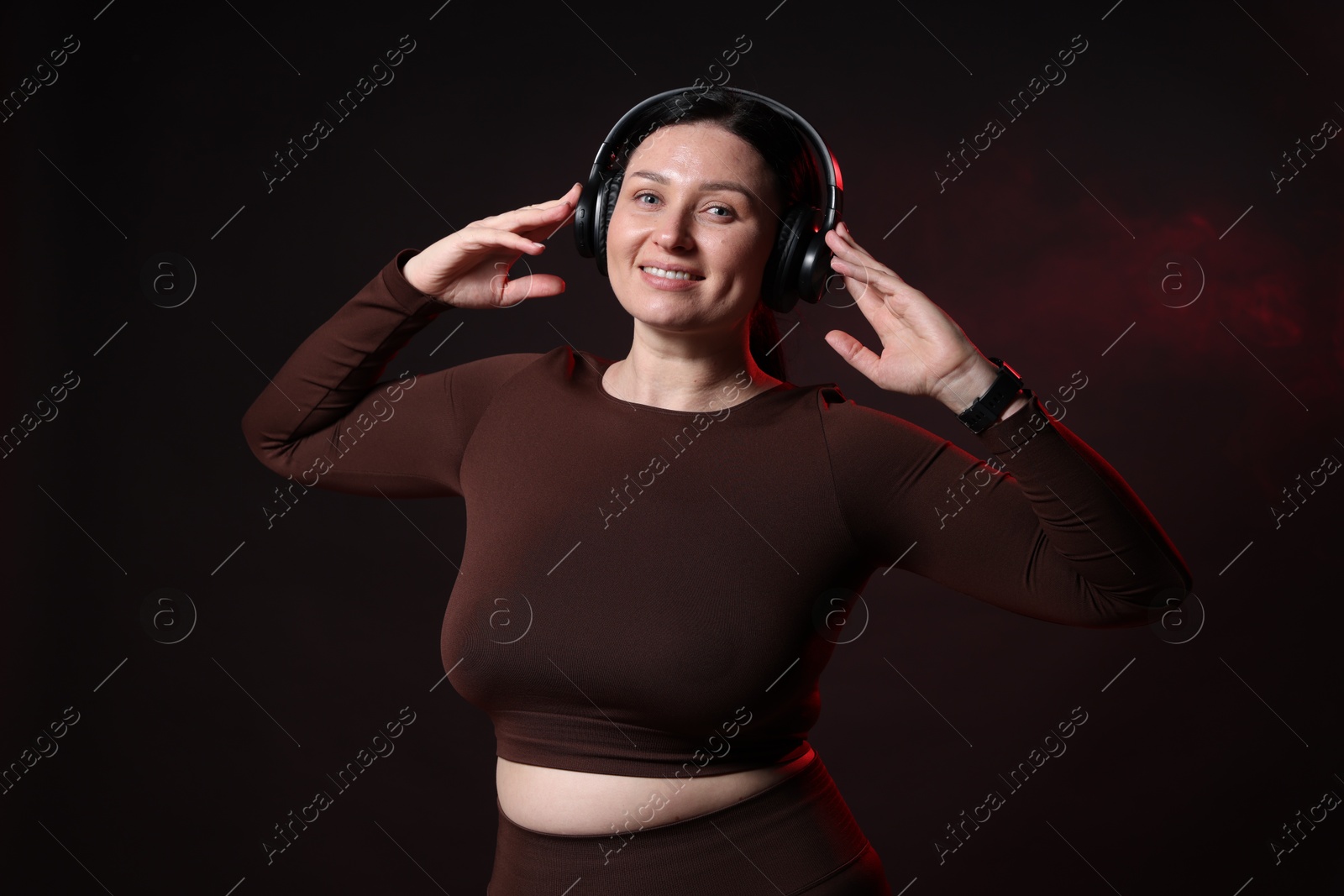 Photo of Plus size woman in gym clothes and headphones on black background with smoke