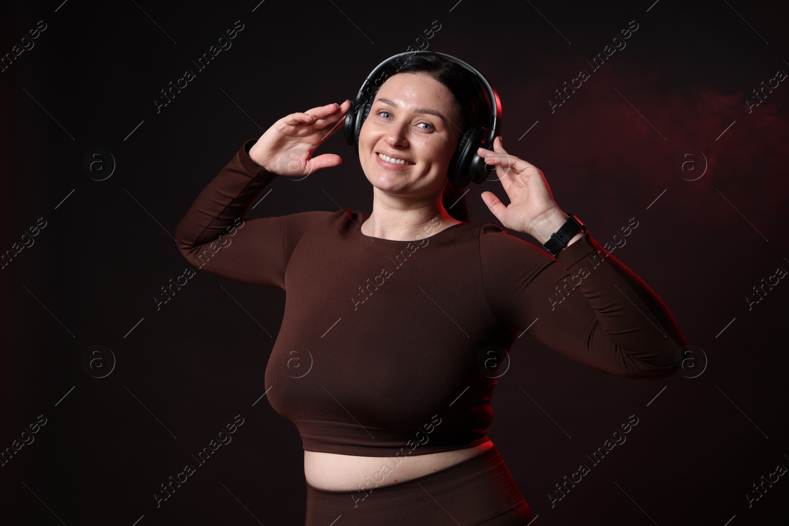 Photo of Plus size woman in gym clothes and headphones on black background with smoke