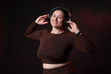 Photo of Plus size woman in gym clothes and headphones on black background with smoke