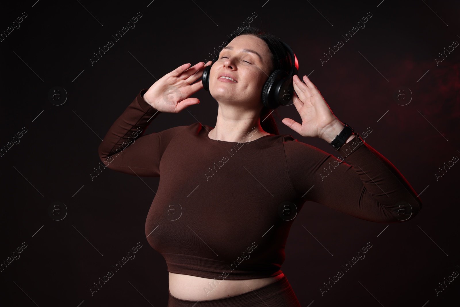 Photo of Plus size woman in gym clothes and headphones on black background with smoke