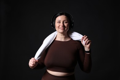 Photo of Plus size woman in gym clothes with headphones and towel on black background