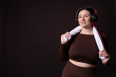 Photo of Plus size woman in gym clothes with headphones and towel on black background, space for text