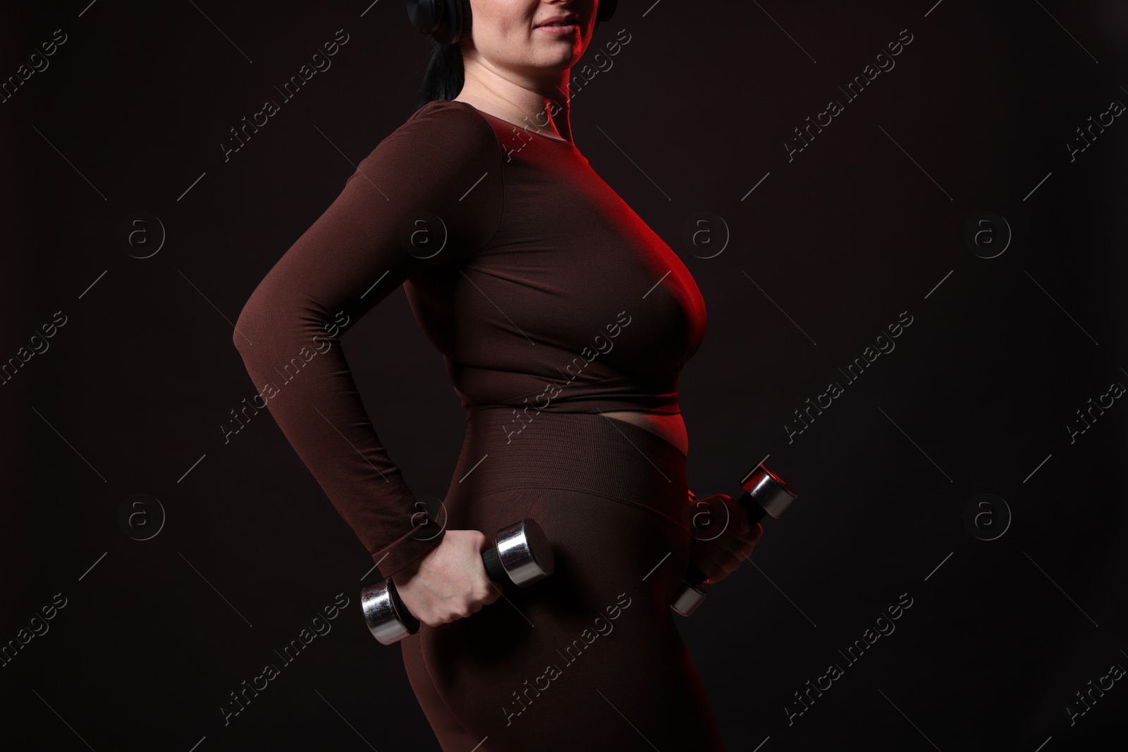 Photo of Plus size woman in gym clothes with dumbbells on black background, closeup