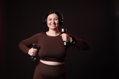 Photo of Plus size woman in gym clothes with dumbbells and headphones on black background