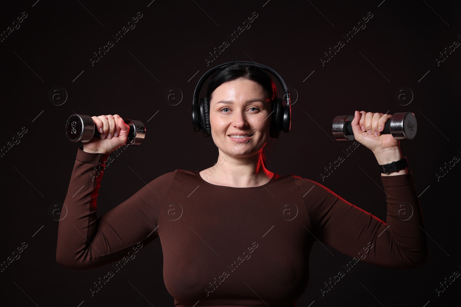 Photo of Plus size woman in gym clothes with dumbbells and headphones on black background