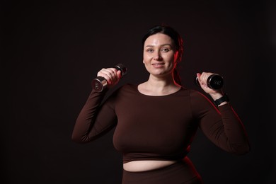 Photo of Plus size woman in gym clothes with dumbbells on black background, space for text