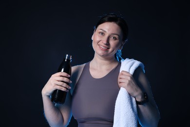 Photo of Plus size woman in gym clothes with water bottle and towel on black background