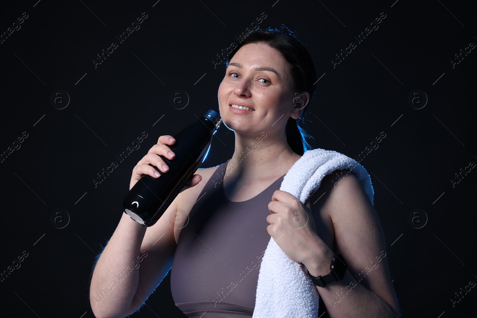 Photo of Plus size woman in gym clothes with water bottle and towel on black background