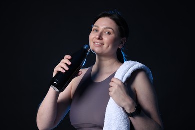 Photo of Plus size woman in gym clothes with water bottle and towel on black background