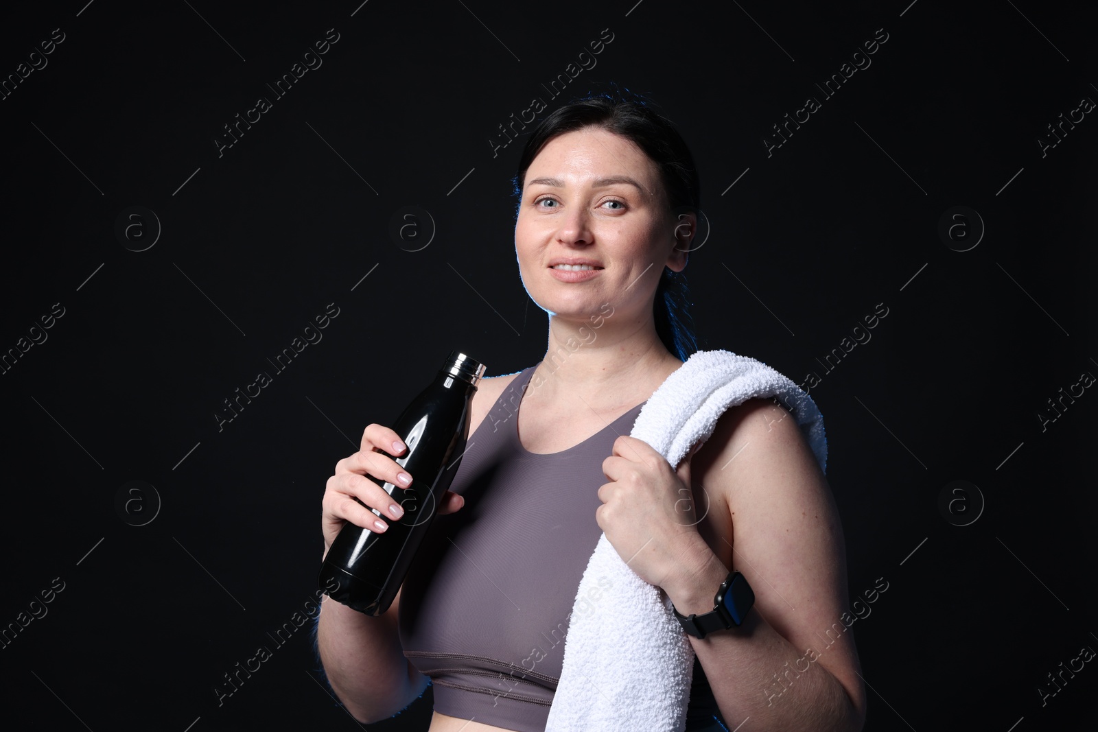 Photo of Plus size woman in gym clothes with water bottle and towel on black background