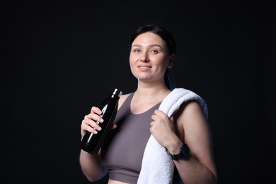 Photo of Plus size woman in gym clothes with water bottle and towel on black background