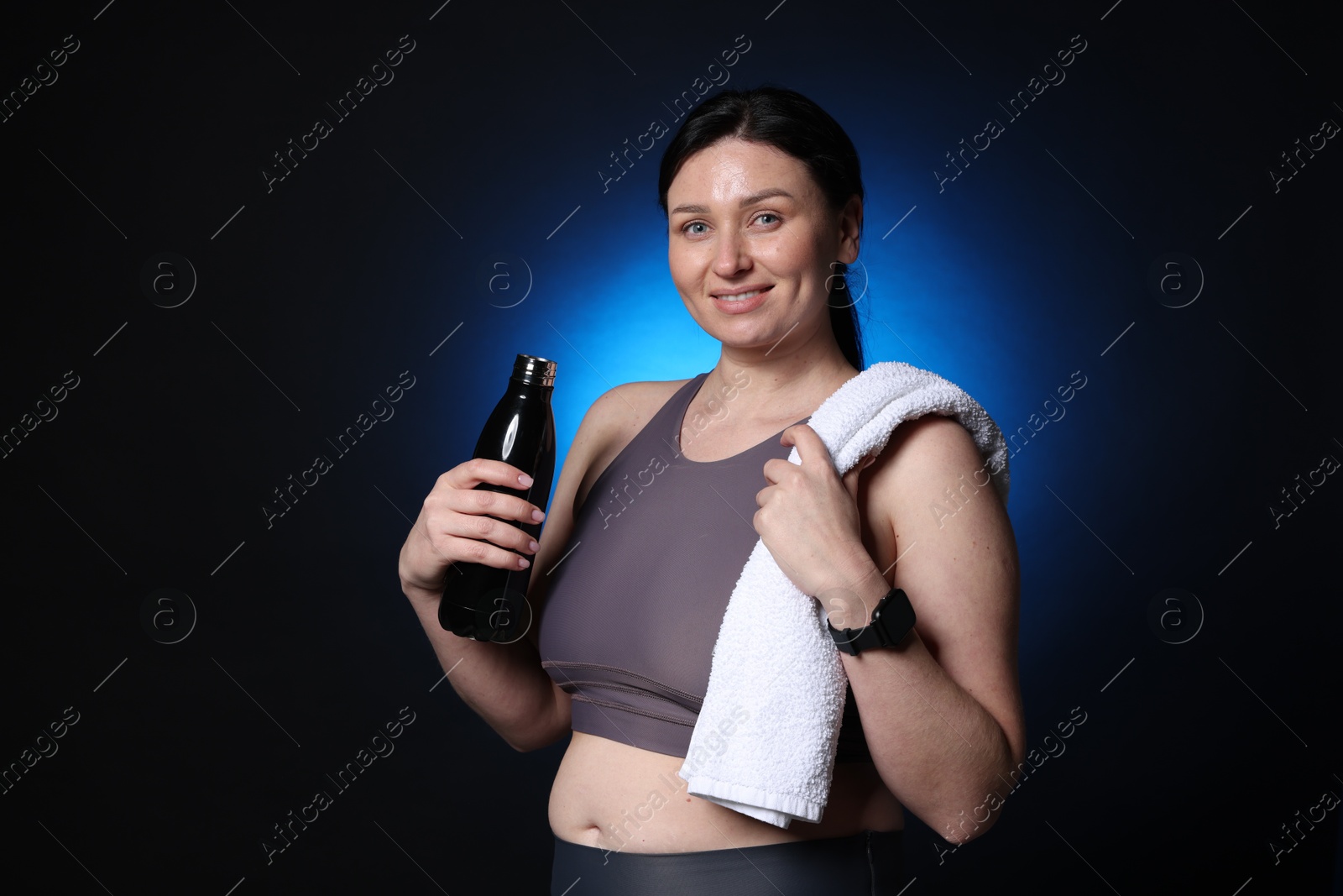 Photo of Plus size woman in gym clothes with water bottle and towel on dark blue background