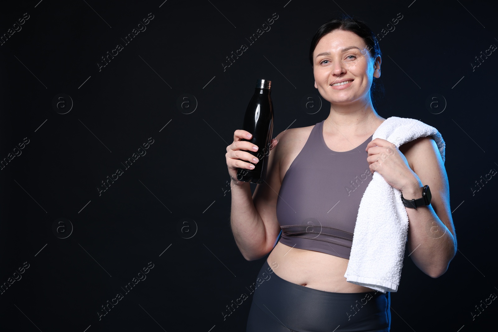 Photo of Plus size woman in gym clothes with water bottle and towel on black background