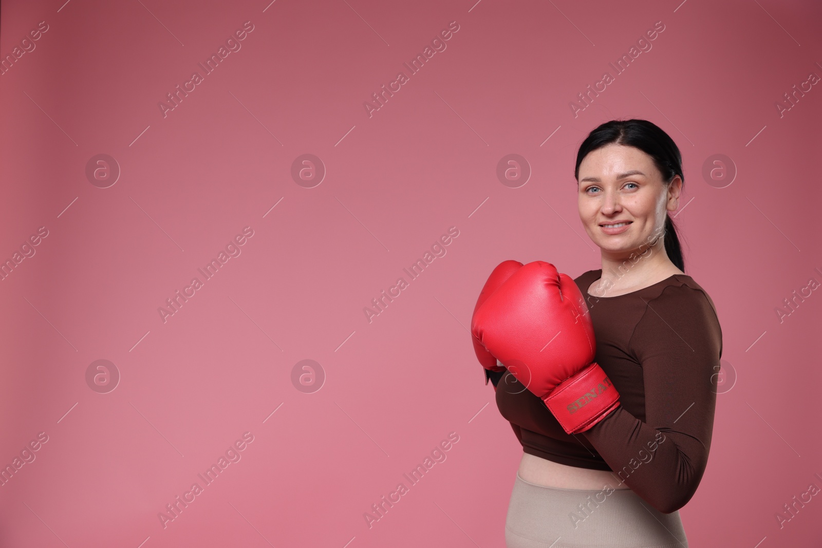 Photo of Plus size woman in gym clothes with boxing gloves on pink background, space for text