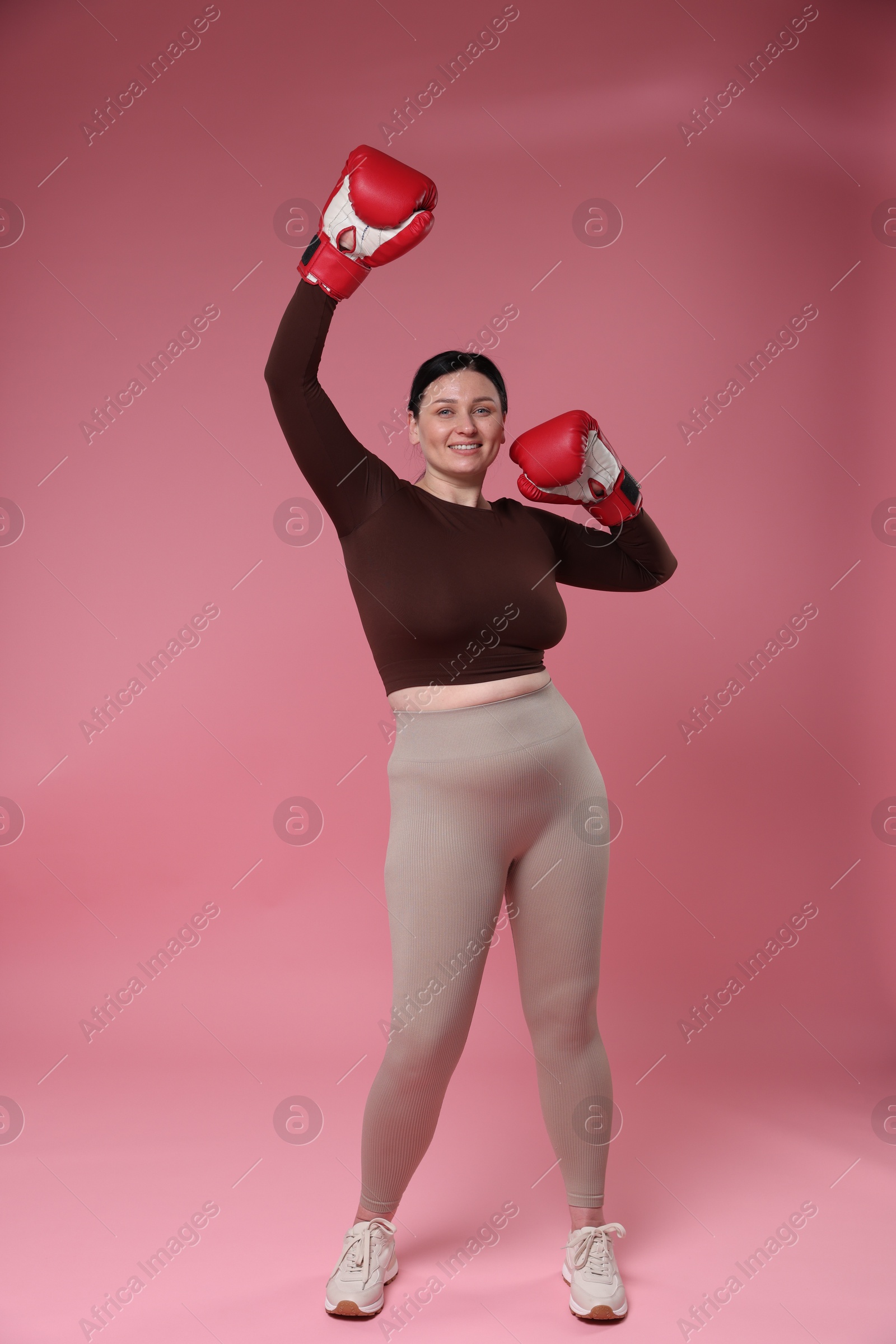 Photo of Plus size woman in gym clothes with boxing gloves on pink background