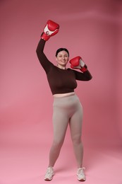 Photo of Plus size woman in gym clothes with boxing gloves on pink background