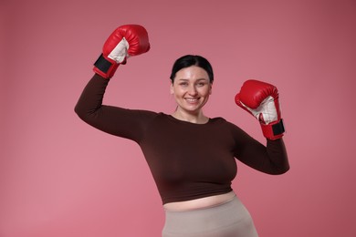 Photo of Plus size woman in gym clothes with boxing gloves on pink background