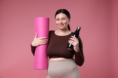 Photo of Plus size woman in gym clothes with fitness mat and water bottle on pink background