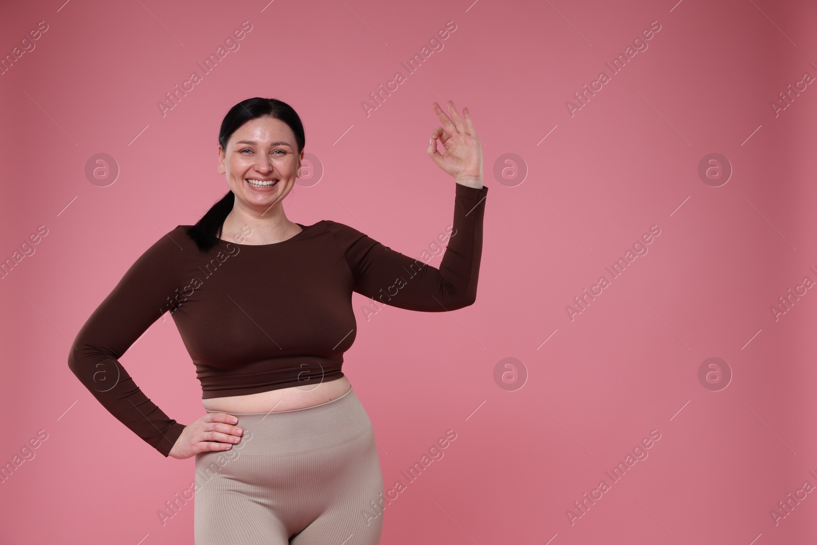 Photo of Plus size woman in gym clothes showing ok gesture on pink background, space for text