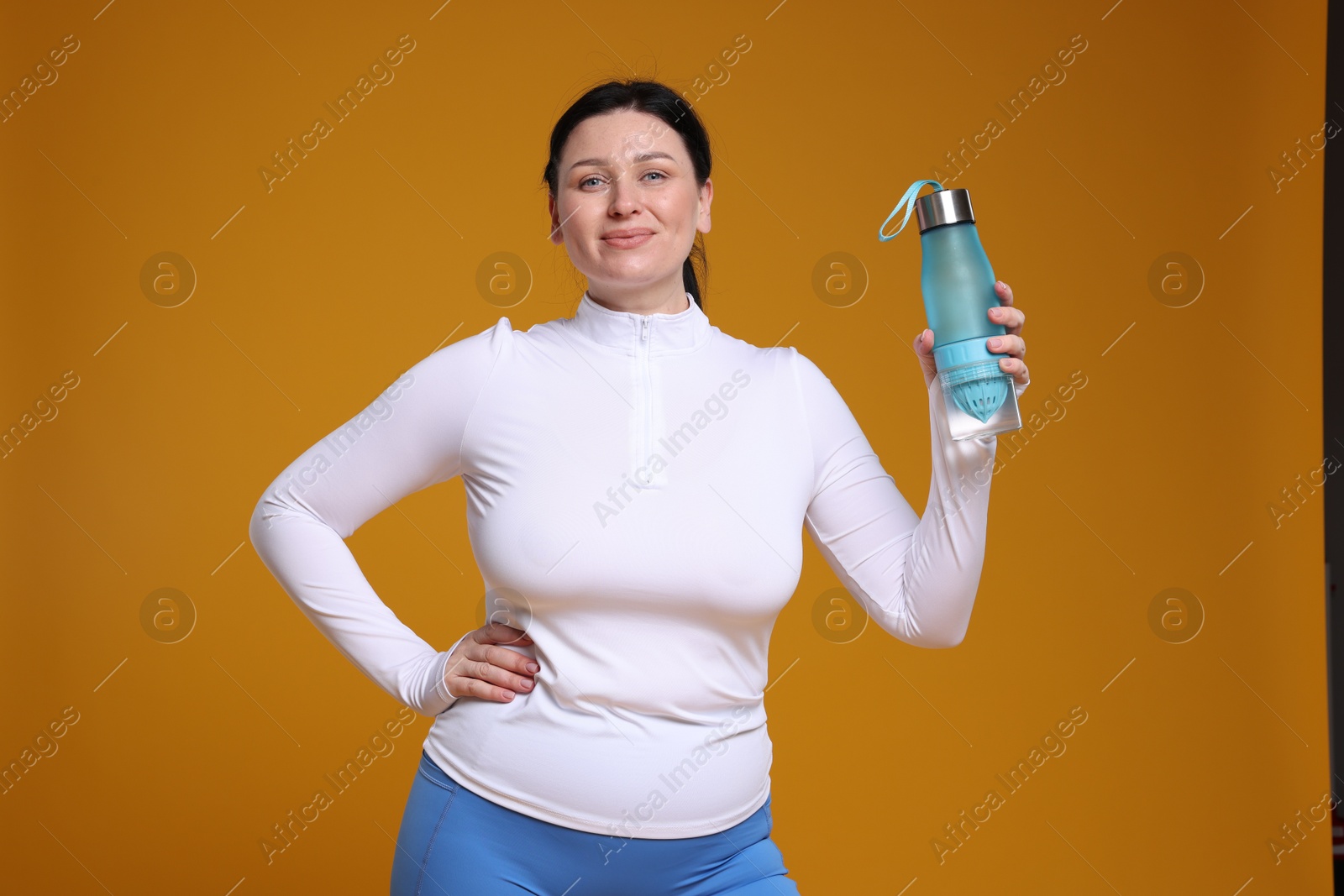 Photo of Plus size woman in gym clothes with water bottle on orange background