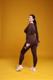 Photo of Plus size woman in gym clothes with dumbbells on orange background