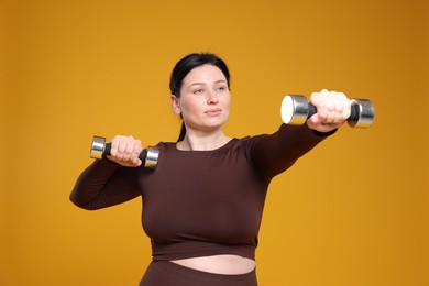 Photo of Plus size woman in gym clothes with dumbbells on orange background