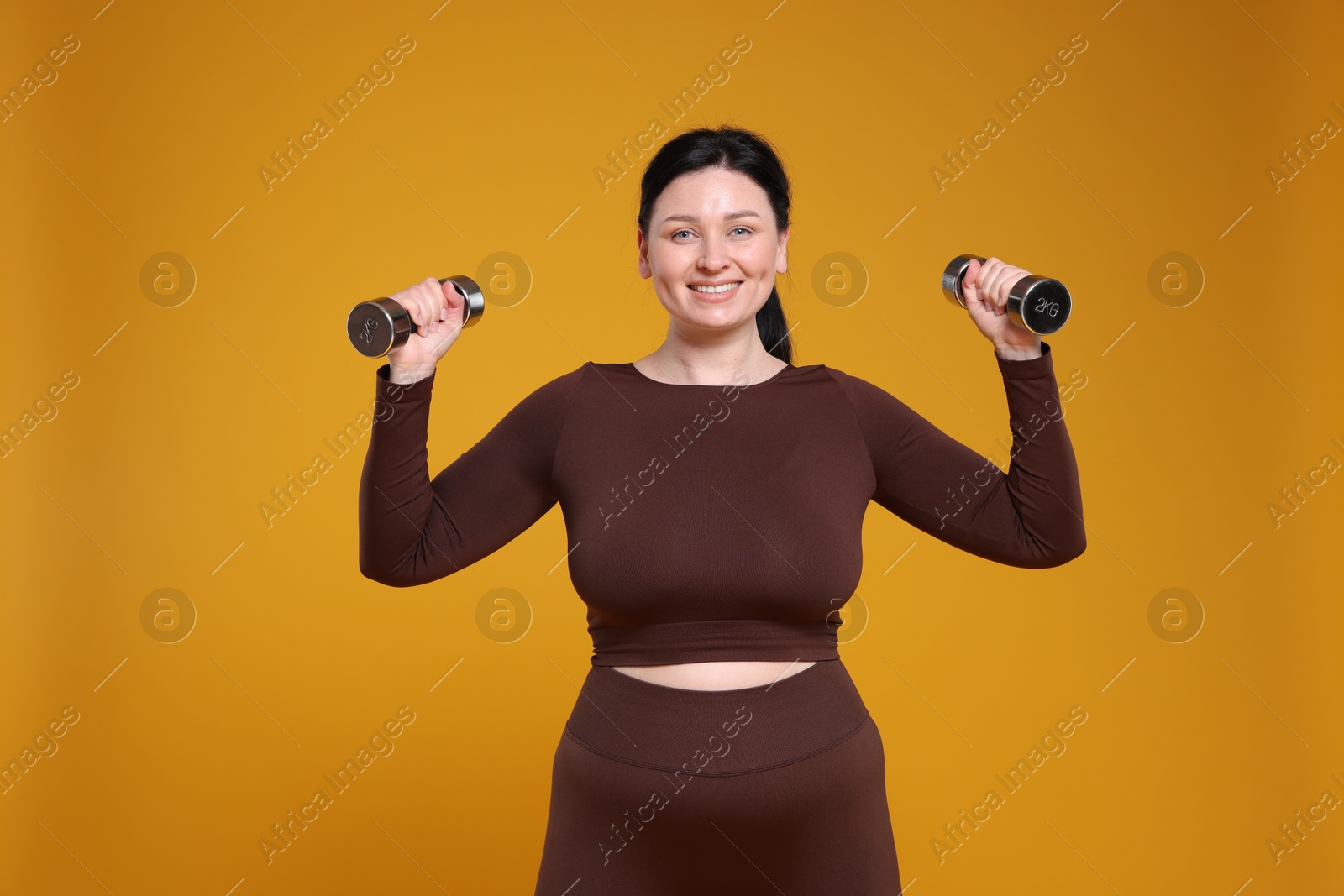 Photo of Plus size woman in gym clothes with dumbbells on orange background