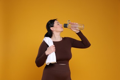 Photo of Plus size woman in gym clothes drinking water on orange background