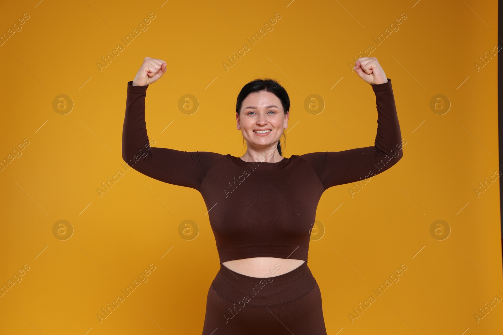 Photo of Plus size woman in gym clothes showing her biceps on orange background