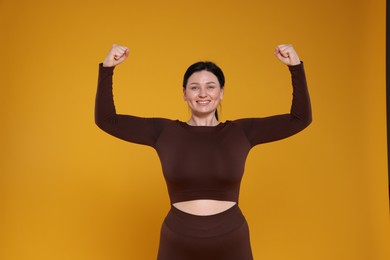 Photo of Plus size woman in gym clothes showing her biceps on orange background