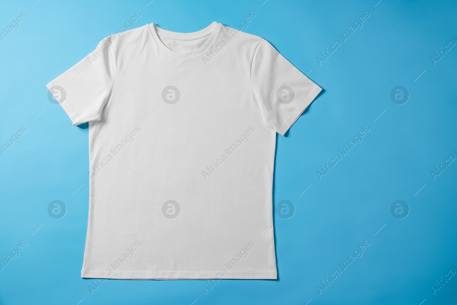 Photo of One blank t-shirt on light blue background, top view. Mockup for design