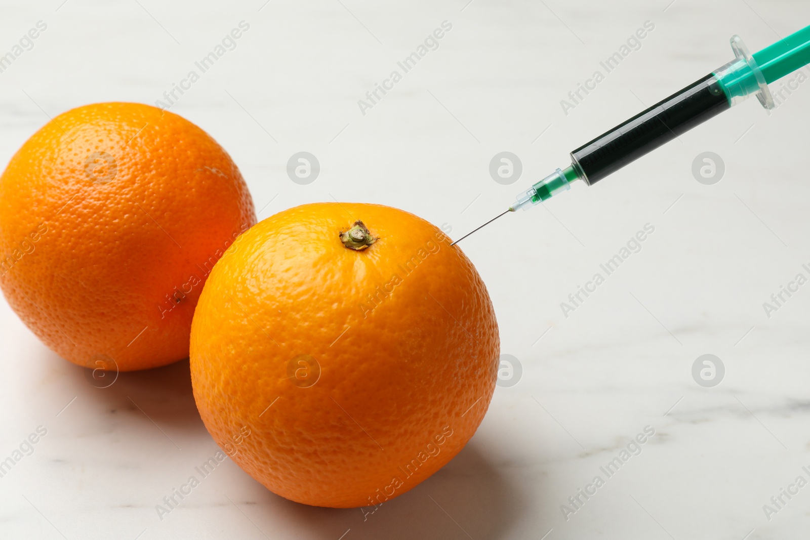 Photo of GMO concept. Injecting orange with syringe at white marble table, closeup