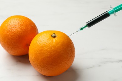 Photo of GMO concept. Injecting orange with syringe at white marble table, closeup