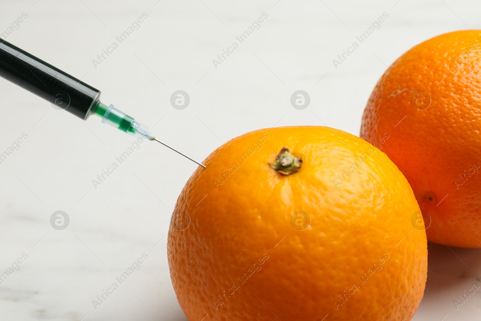 Photo of GMO concept. Injecting orange with syringe at white table, closeup